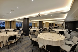 Un salón de conferencias con varias mesas redondas, cada una dispuesta con sillas y vajilla, en un hotel moderno.