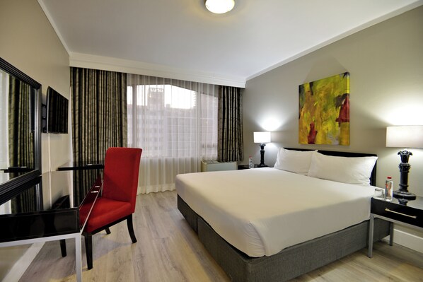 A hotel room with a large bed, a red chair, a desk, and a TV.