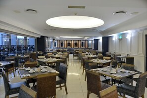 A spacious restaurant with multiple dining tables and chairs, large windows, and a modern ceiling design. - Capetonian Hotel (Cape Town)