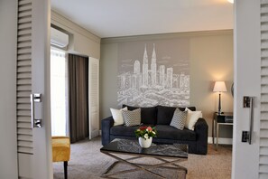 Una sala de estar moderna con un sofá oscuro, una mesa de centro y un mural con un paisaje urbano en la pared.