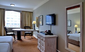 Una habitación de hotel con cama, escritorio, silla, cómoda, televisor y un espejo grande.