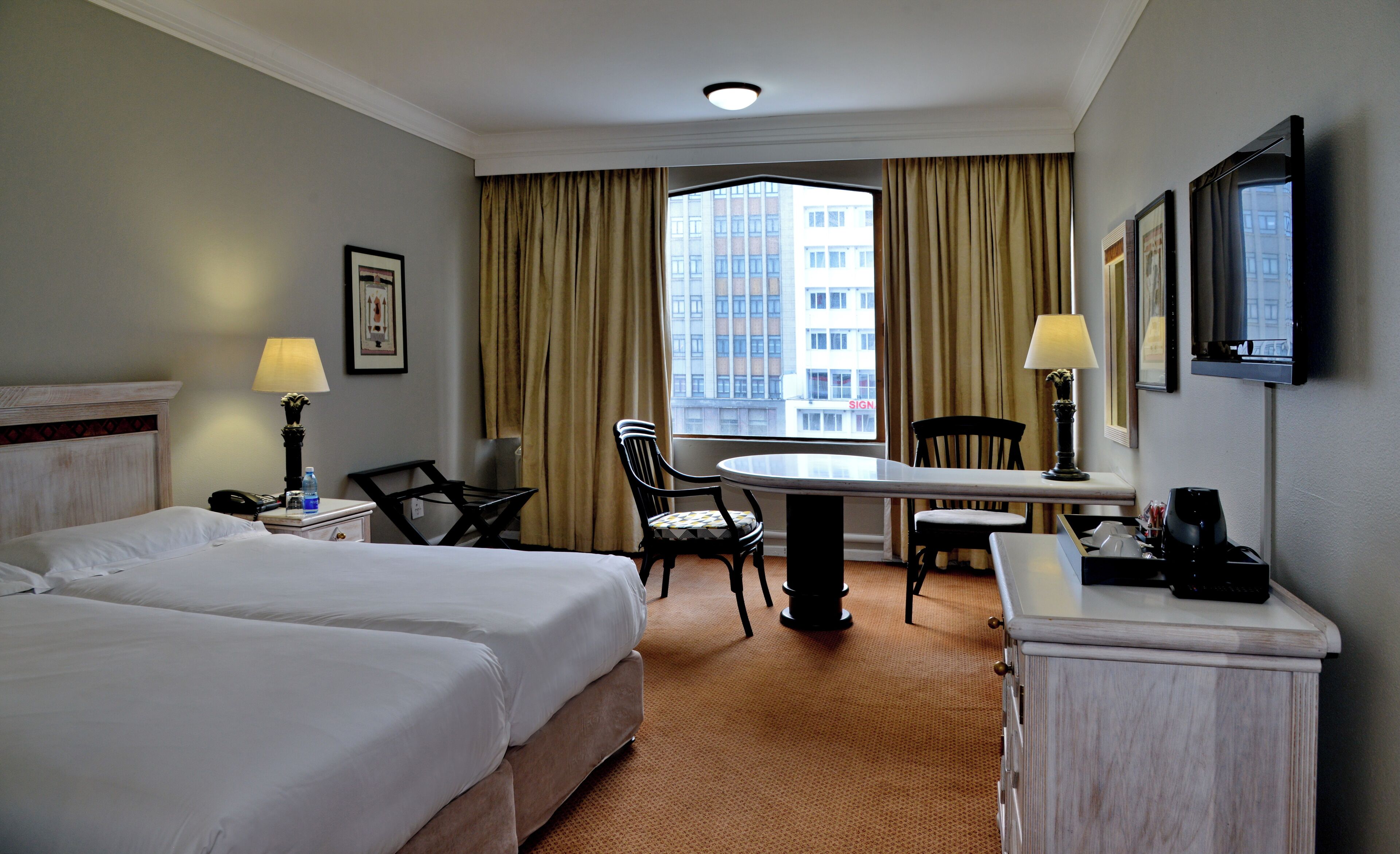 A hotel room with two beds, a desk, a chair, a lamp, a TV, and a window with curtains.