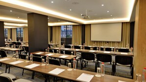 A conference room with multiple tables, chairs, and a projector screen. - Capetonian Hotel (Cape Town)