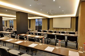 A conference room with multiple tables, chairs, and a projector screen. - Capetonian Hotel (Cape Town)