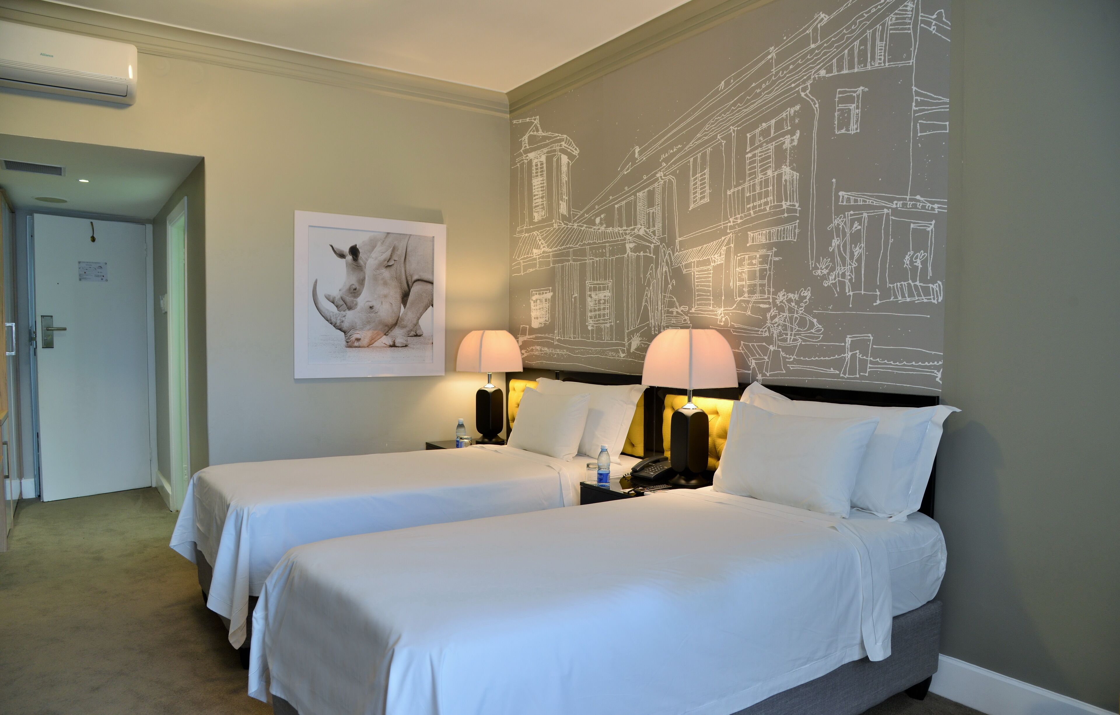 A hotel room with two beds, a wall mural, a framed animal picture, and bedside lamps.