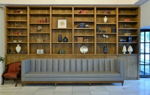 A room with a large wooden bookshelf filled with books and decorative items, a grey sofa, and a red chair.
