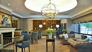 A spacious living room with a fireplace, a large chandelier, and a view of the outdoors. - Capetonian Hotel (Cape Town)
