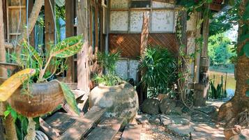 A rustic wooden structure with a thatched roof, surrounded by greenery and a small stream.
