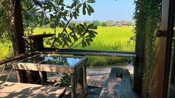 A wooden deck with a glass table and benches, overlooking a green field and houses in the distance.