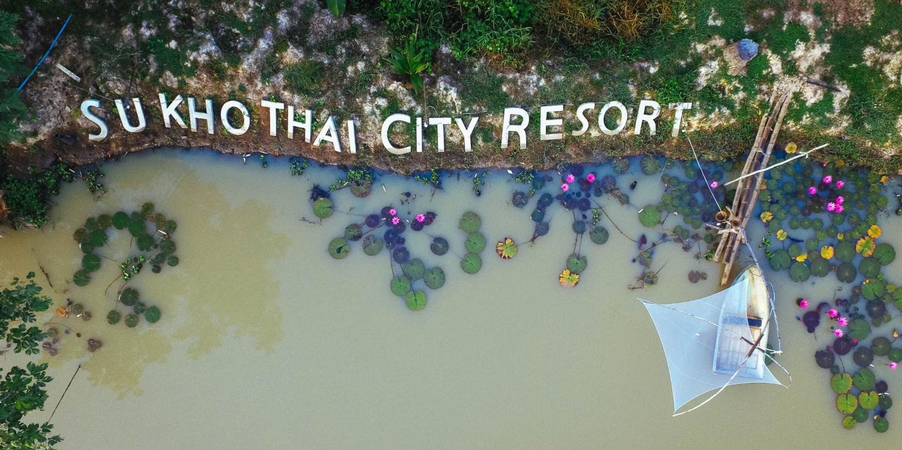 Vista aérea del Su Kho Thai City Resort, con una masa de agua, plantas flotantes y un pequeño bote.