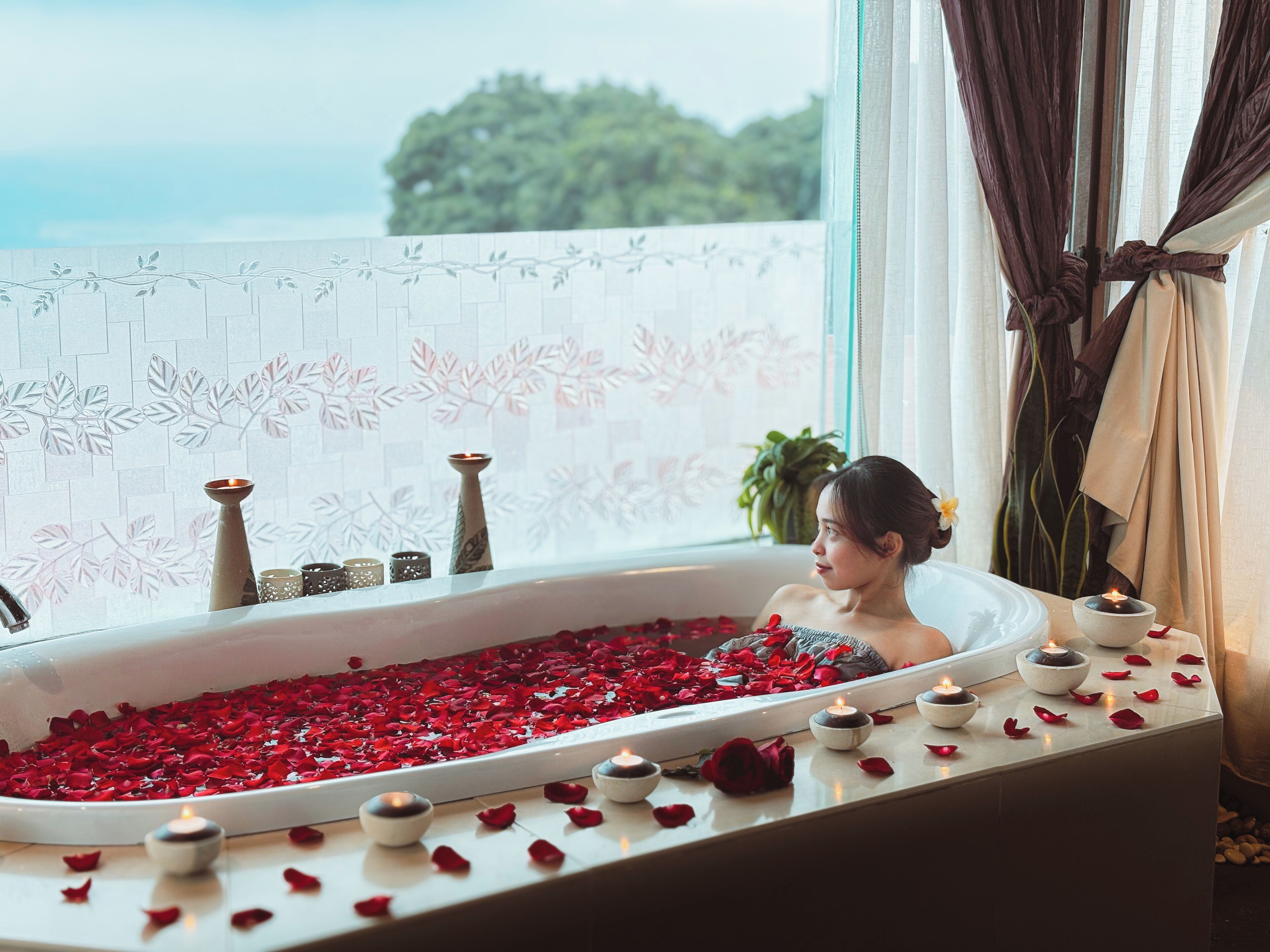 Una bañera llena de pétalos de rosa y velas, con vistas a zonas verdes.