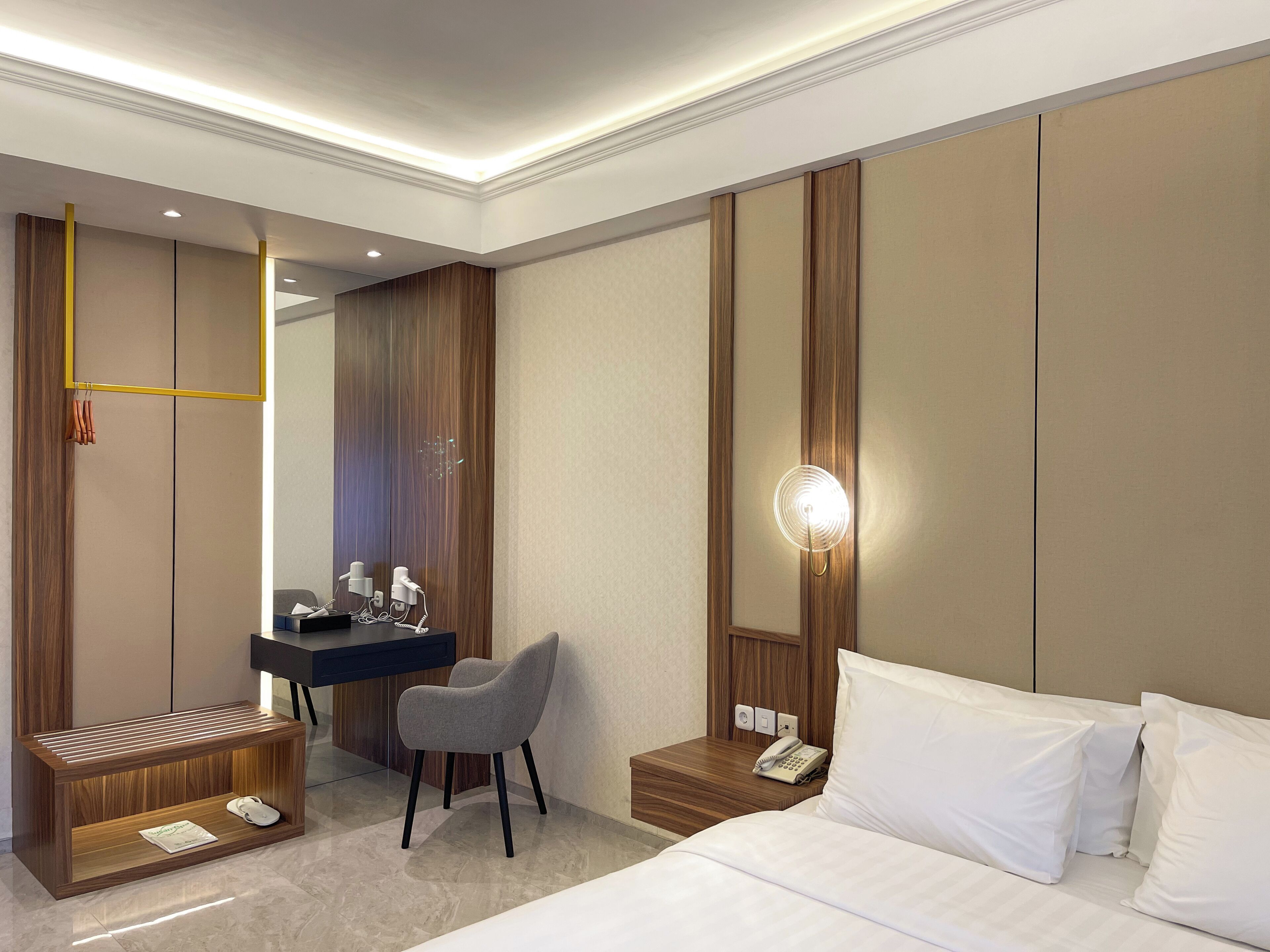 Una habitación de hotel con una cama, un escritorio con una silla, un tocador con espejo y una mesita de noche con teléfono.