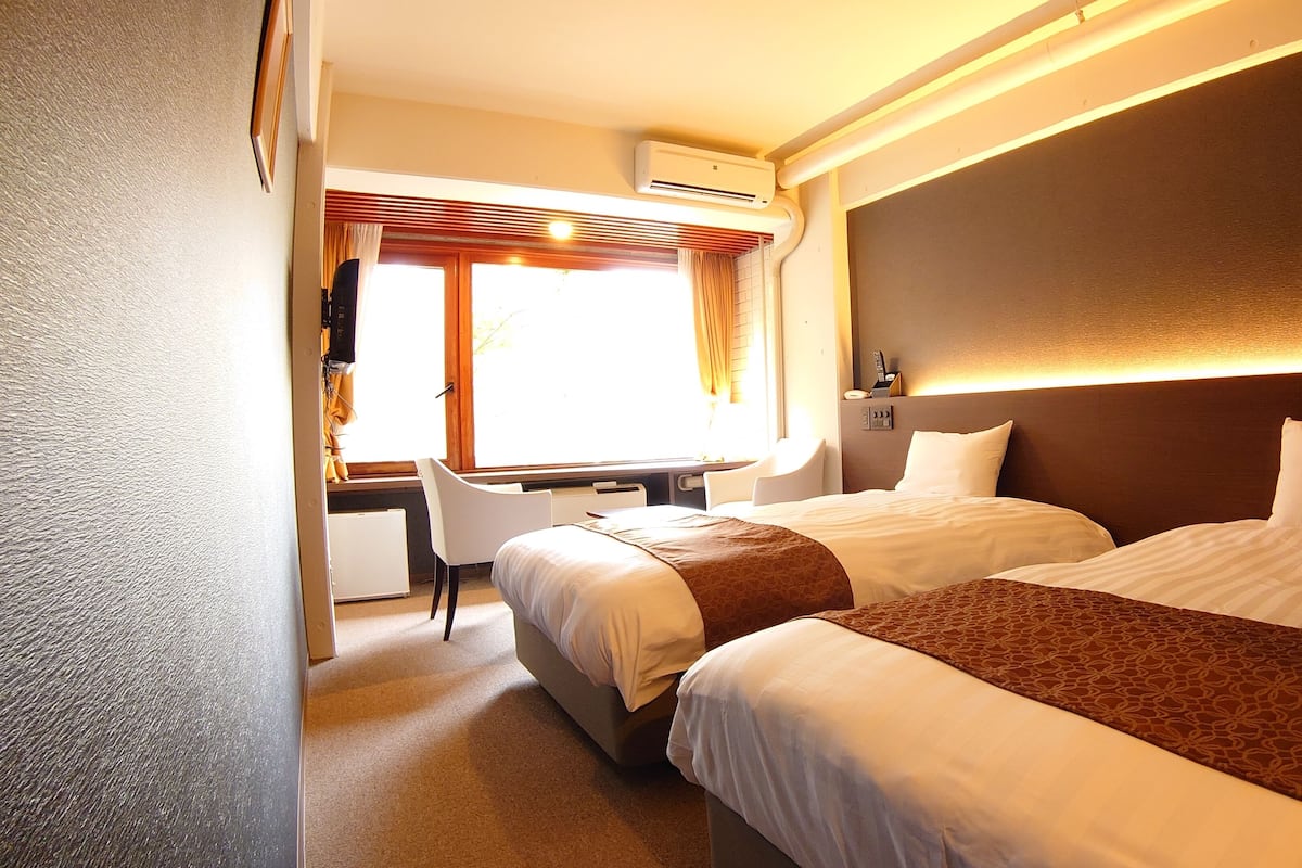 Une chambre d’hôtel avec deux lits, un bureau et une fenêtre avec des rideaux.