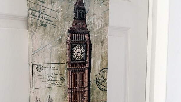 A door with a vintage-style wall hanging depicting the Big Ben clock tower. - Metropoli Suites Ejecutivas (Puebla)