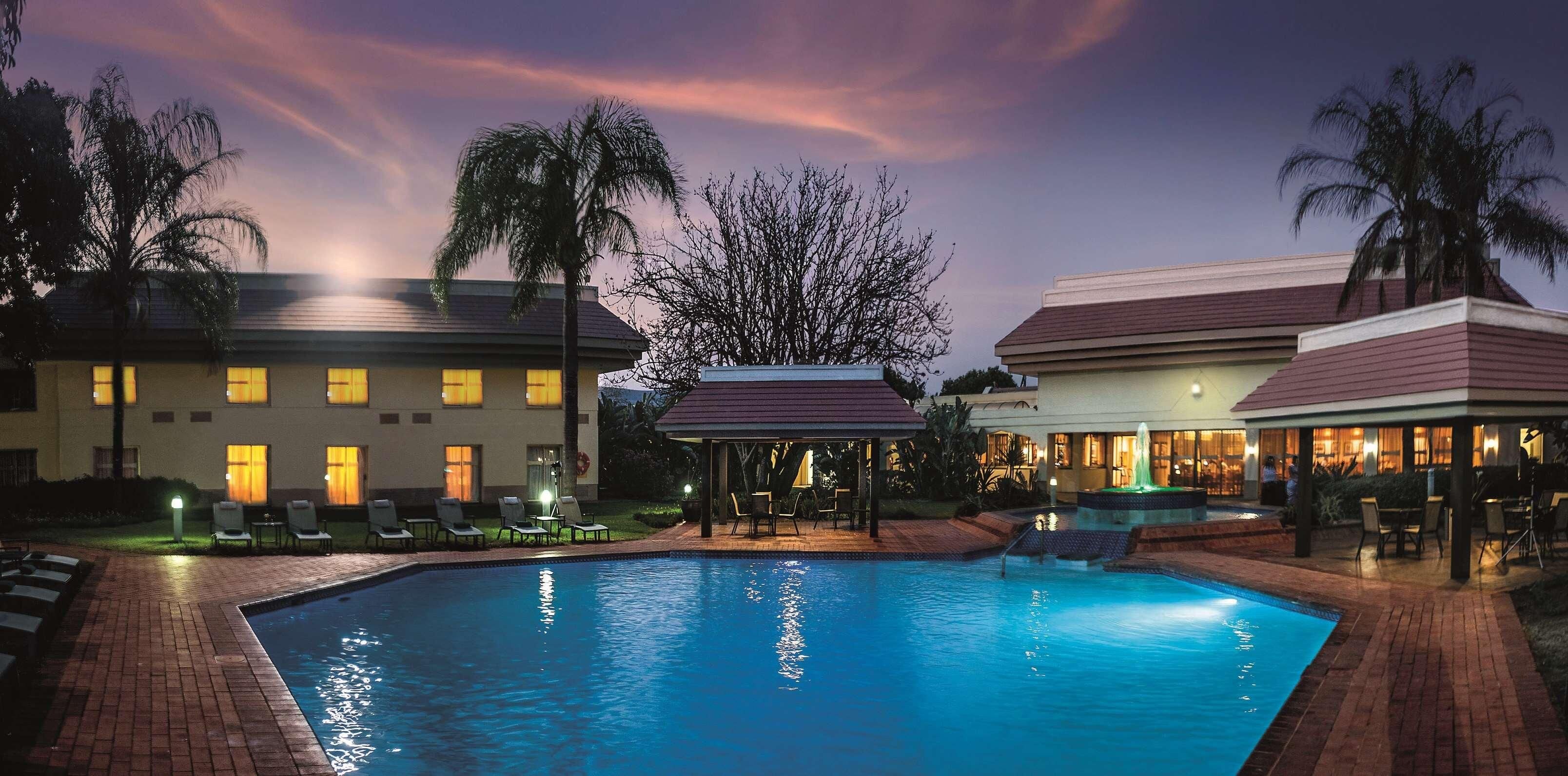 A hotel with a swimming pool, lounge chairs, and a gazebo.