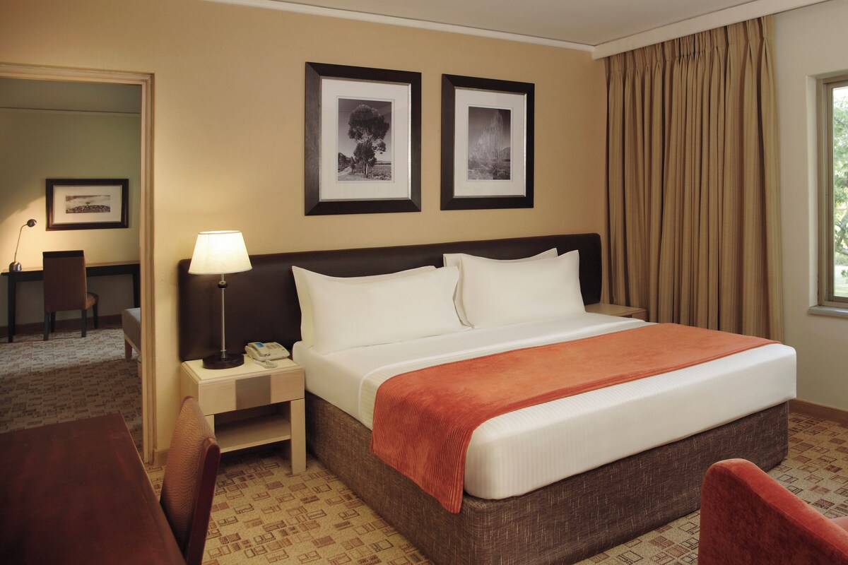 A hotel room with a bed, a desk, a chair, a nightstand, a lamp, and two framed pictures on the wall.