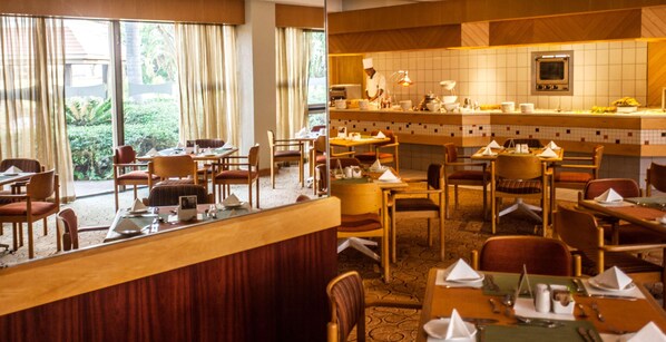 A restaurant with a counter, tables, chairs, and a chef preparing food. - Garden Court Ulundi (Ulundi)