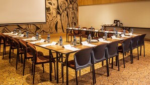 Un salón de conferencias con una larga mesa, sillas, botellas de agua, tarjetas de identificación y una pantalla de proyector.