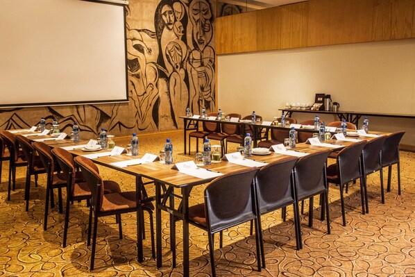 A conference room with a long table, chairs, water bottles, nameplates, and a projector screen. - Garden Court Ulundi (Ulundi)