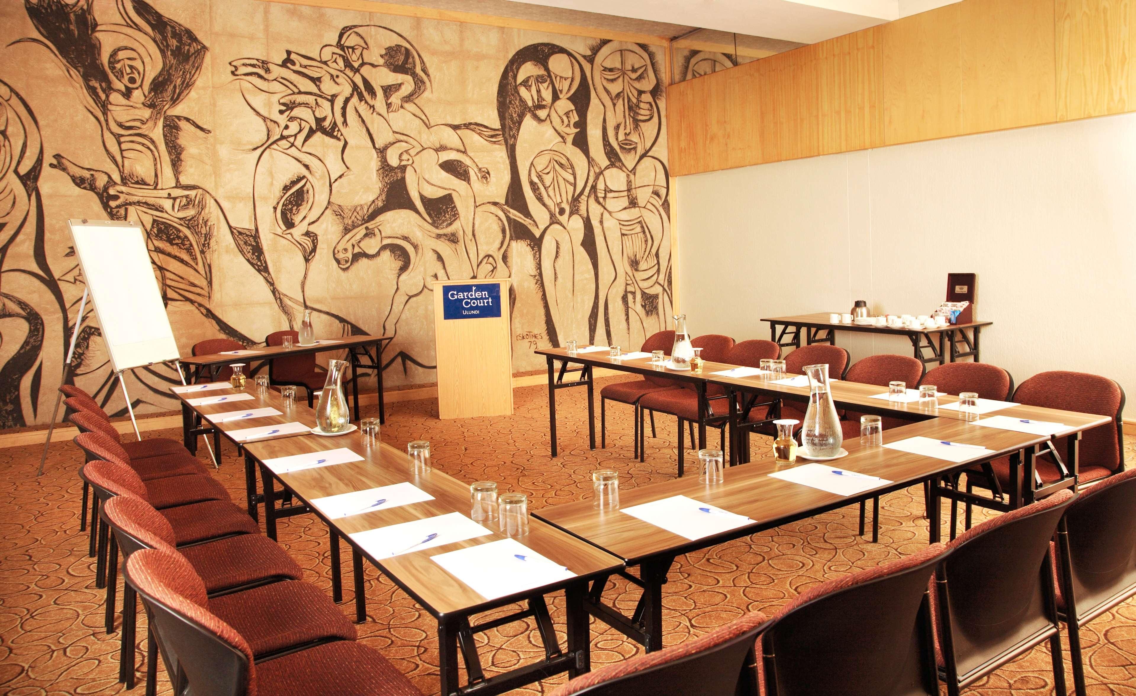 Un salón de conferencias con una larga mesa, sillas y una pizarra. Un mural adorna la pared detrás de la mesa.