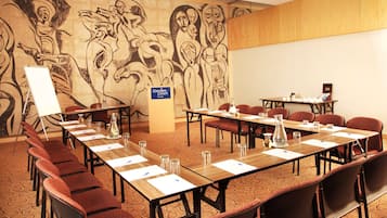 Un salón de conferencias con una larga mesa, sillas y una pizarra. Un mural adorna la pared detrás de la mesa.
