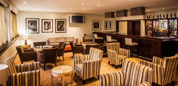 A bar area with a long counter, multiple chairs, a sofa, and a television mounted on the wall. - Garden Court Ulundi (Ulundi)
