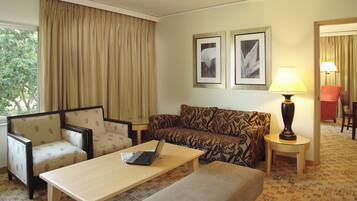 A hotel room with a sofa, armchairs, a small table with a laptop, a lamp, and two framed pictures on the wall.