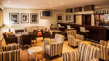A bar area with a long counter, multiple chairs, a sofa, and a television mounted on the wall.