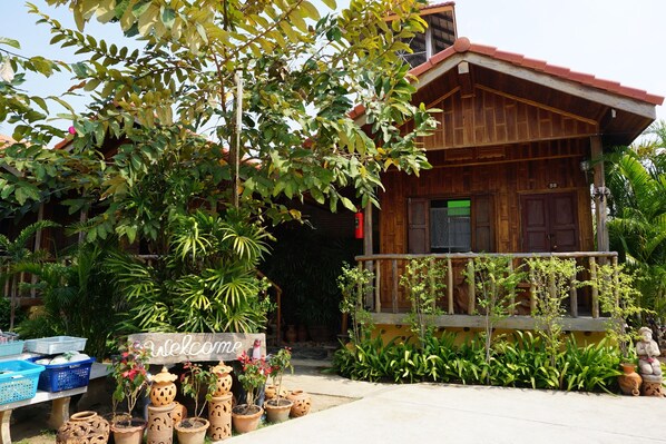 A wooden house with a porch, surrounded by lush greenery and potted plants. - J&J Guesthouse (Sukhothai)