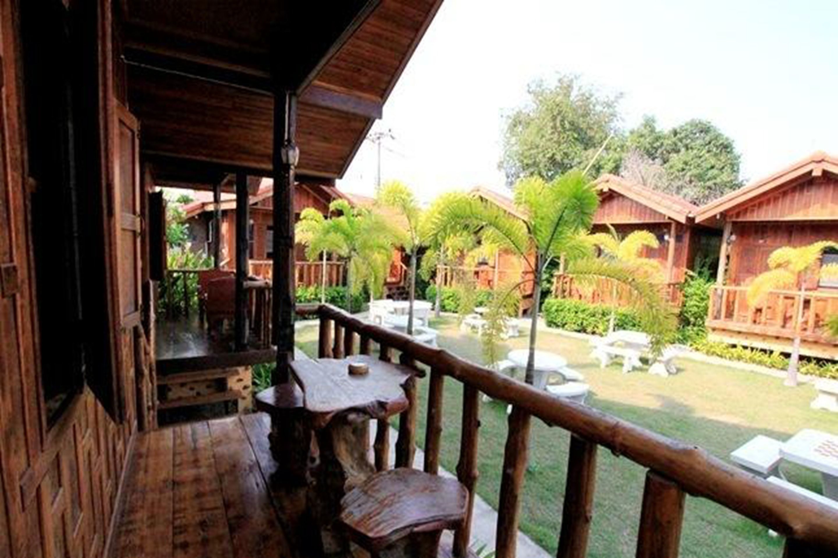 A wooden balcony with a view of a garden area with palm trees and a pool.
