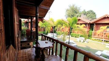A wooden balcony with a view of a garden area with palm trees and a pool.