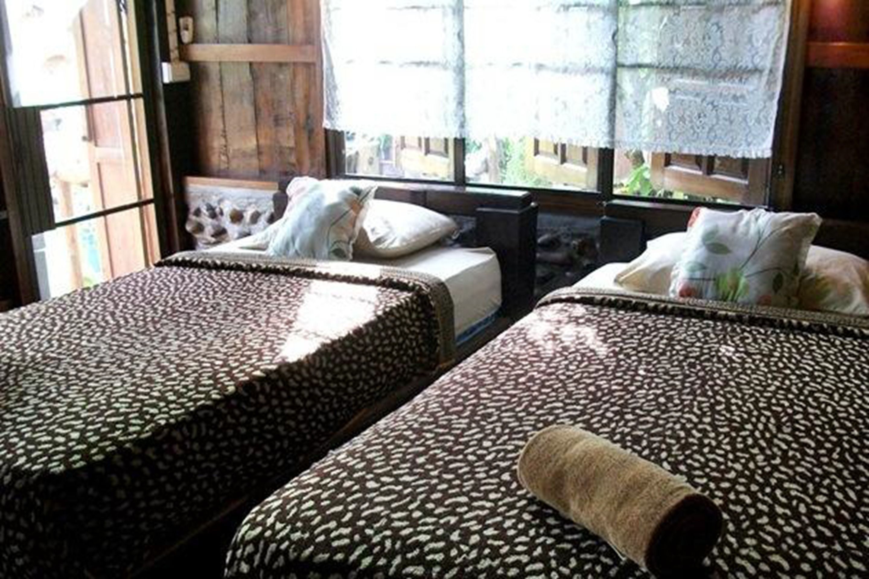 A room with two beds, each with patterned bedding and a rolled towel on one bed.