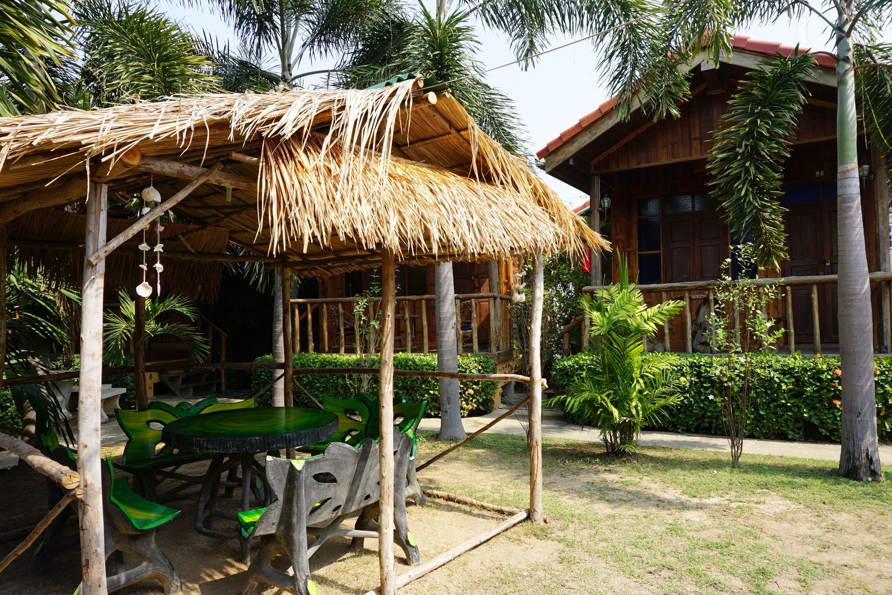 A rustic wooden structure with a thatched roof, surrounded by lush greenery and palm trees.