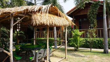 A rustic wooden structure with a thatched roof, surrounded by lush greenery and palm trees.