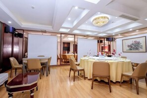 Un salón de conferencias con una mesa redonda, sillas, una pantalla de proyector y una araña.
