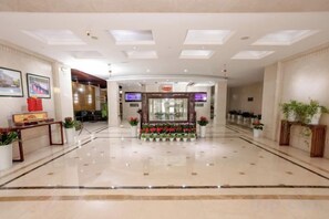 Un hall de hotel con una recepción, una zona de estar con plantas y un suelo pulido.