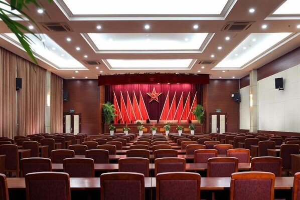 A conference room with rows of chairs, a stage with a red backdrop and a star emblem, and a ceiling with recessed lighting. - Hongqiao Yunfeng Hotel (Shanghai)