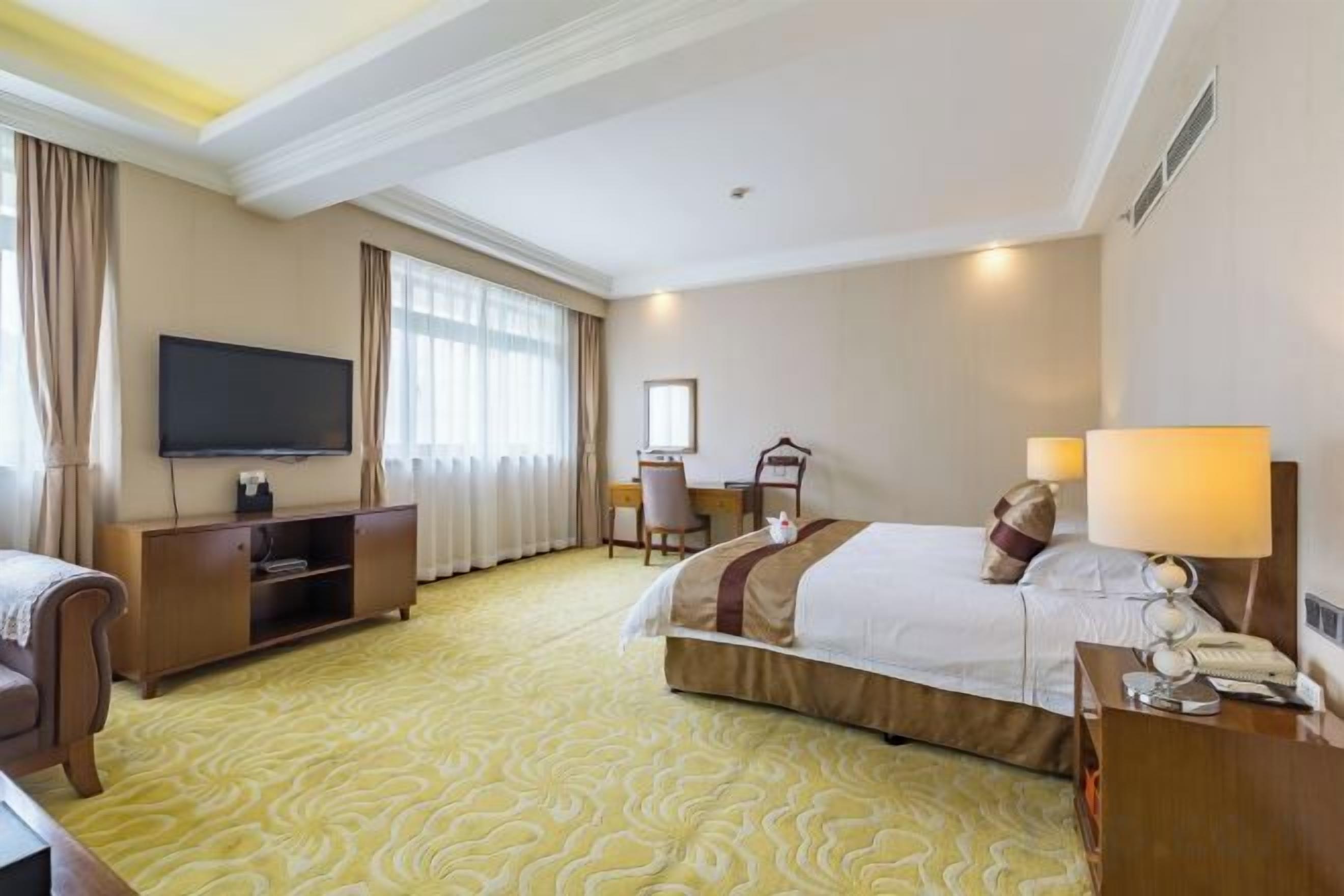 Quarto de hotel com cama, mesas de cabeceira, televisão, escrivaninha e cadeira.