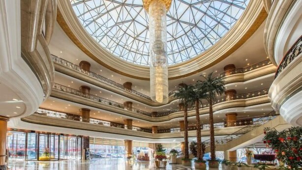 Un atrium à plusieurs niveaux, doté d’une verrière, de nombreux étages et de palmiers.