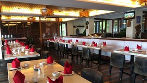 A restaurant with multiple tables, each set with red napkins, white plates, and chopsticks. The room has a modern design with wooden flooring and a bar area in the background. - Jin Jiang Sanya Royal Garden Resort (Sanya)