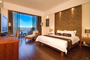Ein geräumiges Schlafzimmer mit einem großen Bett, einem Schreibtisch mit Laptop, einem Sessel und einem Balkon mit Aussicht.
