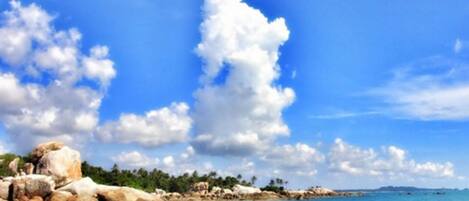 A rocky shoreline with clear water and a blue sky with clouds.