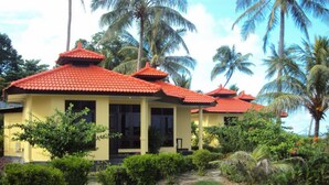 Un bâtiment jaune surmonté d’un toit en tuiles rouges, entouré d’une végétation luxuriante et de palmiers.