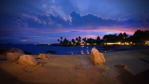 Une plage avec de gros rochers, une mer calme et un ciel au coucher du soleil.