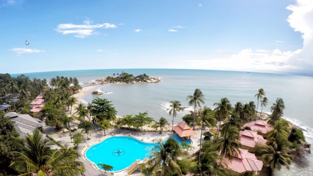 Un complexe hôtelier doté d’une piscine, de palmiers et d’une plage.