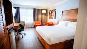 A hotel room with a large bed, a desk with a chair, two smaller chairs, a lamp, and a painting on the wall. - Hôtel Lindbergh par JARO (Québec City)