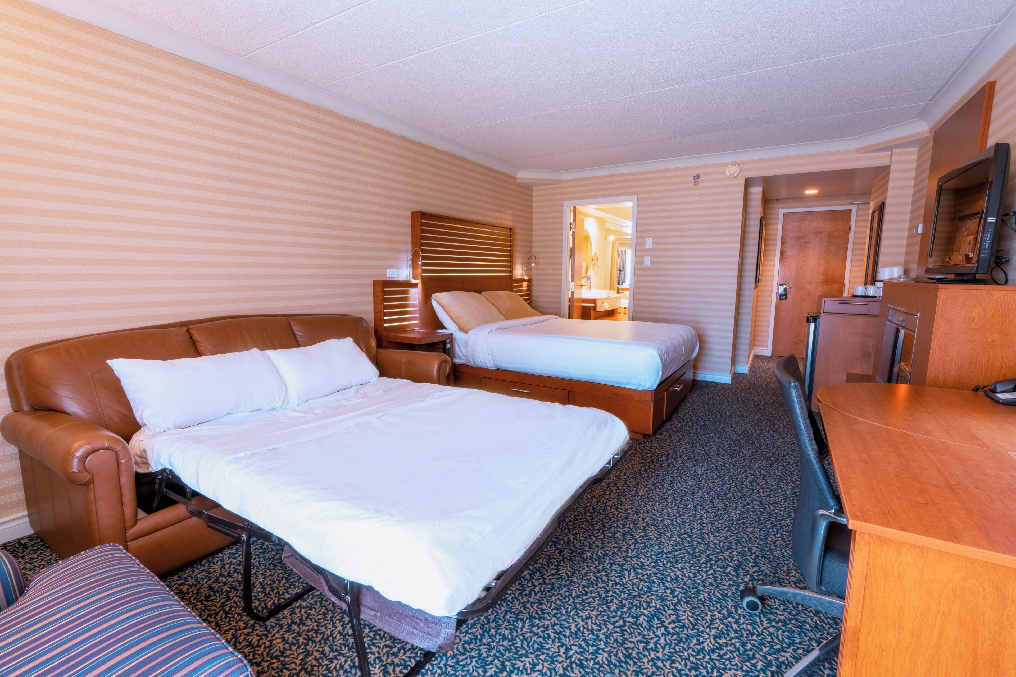 Quarto de hotel com duas camas, um sofá, uma escrivaninha e uma televisão.