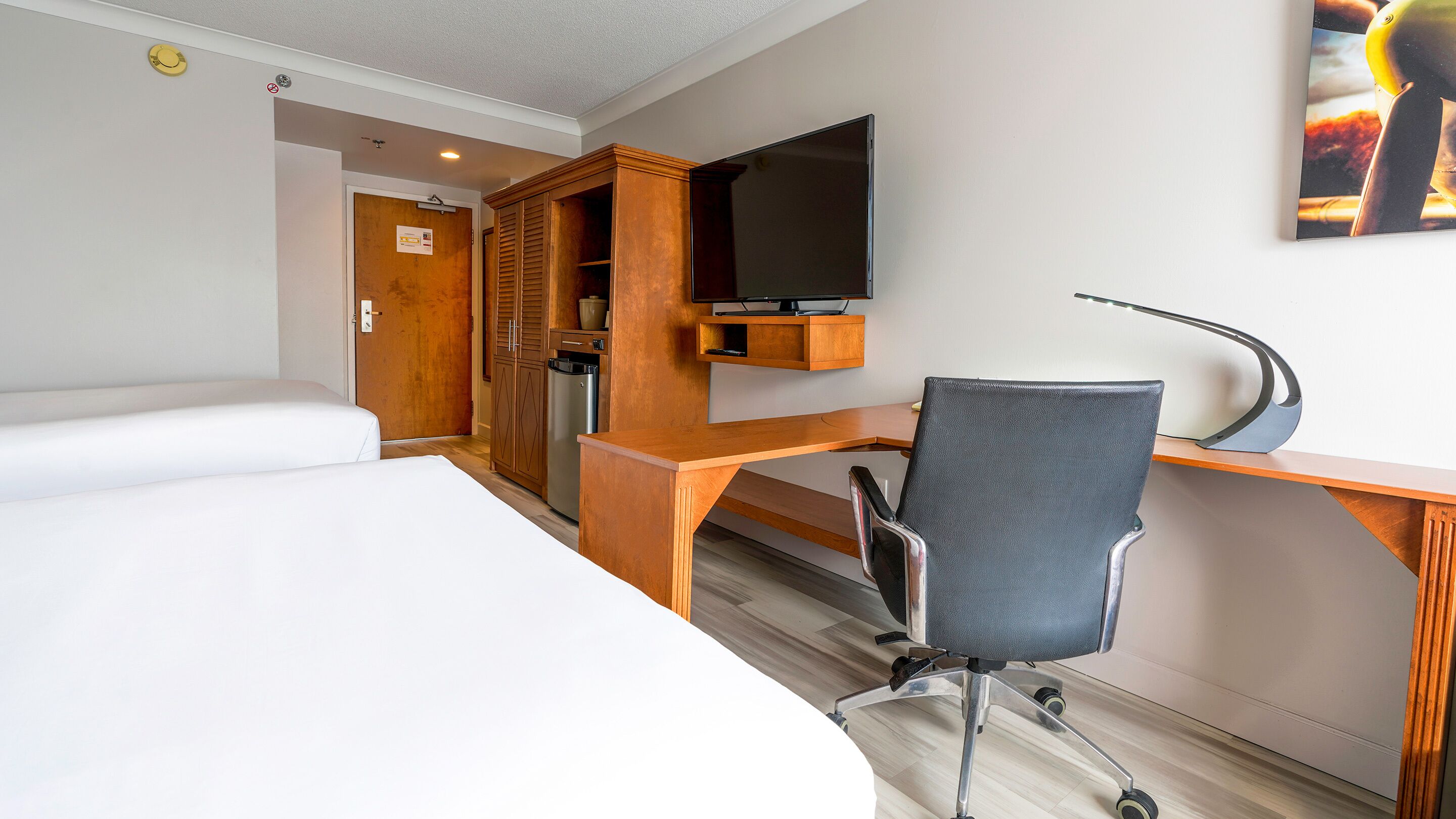 Una habitación de hotel con una cama, un escritorio con silla, televisión y armario.