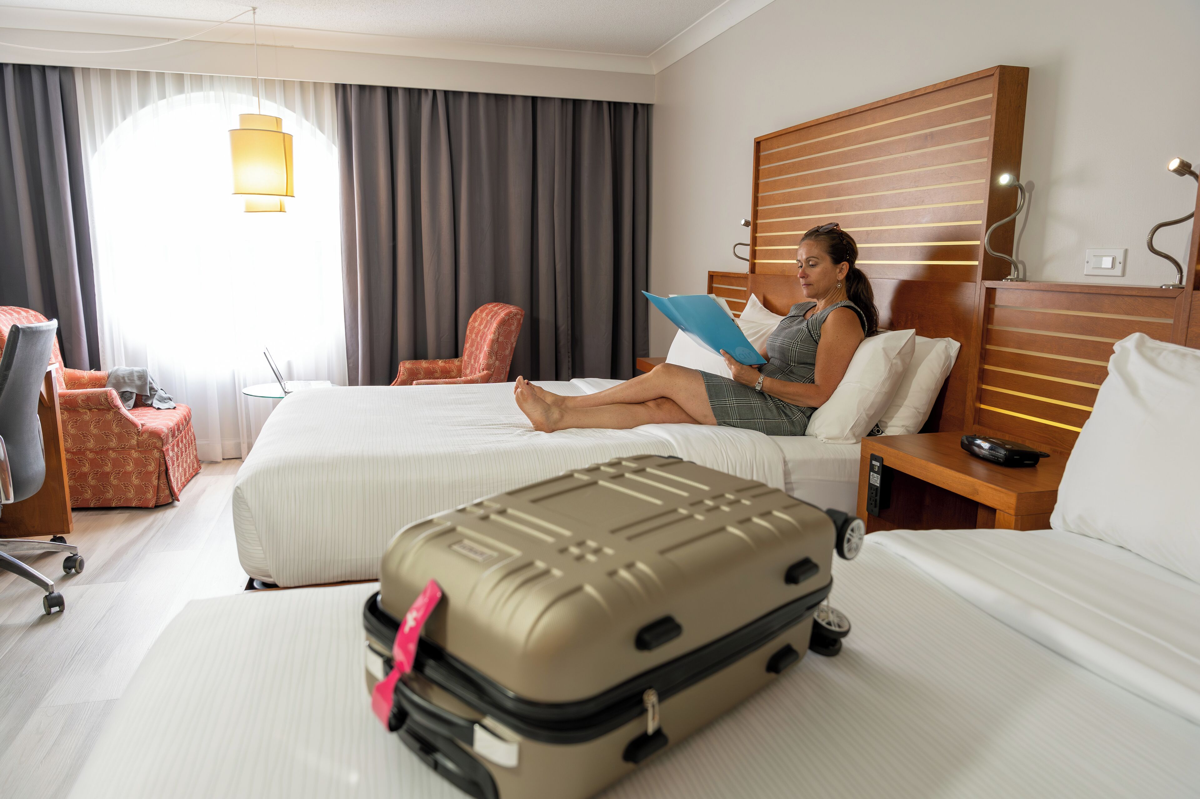 A hotel room with a bed, a suitcase, a desk, and a chair.