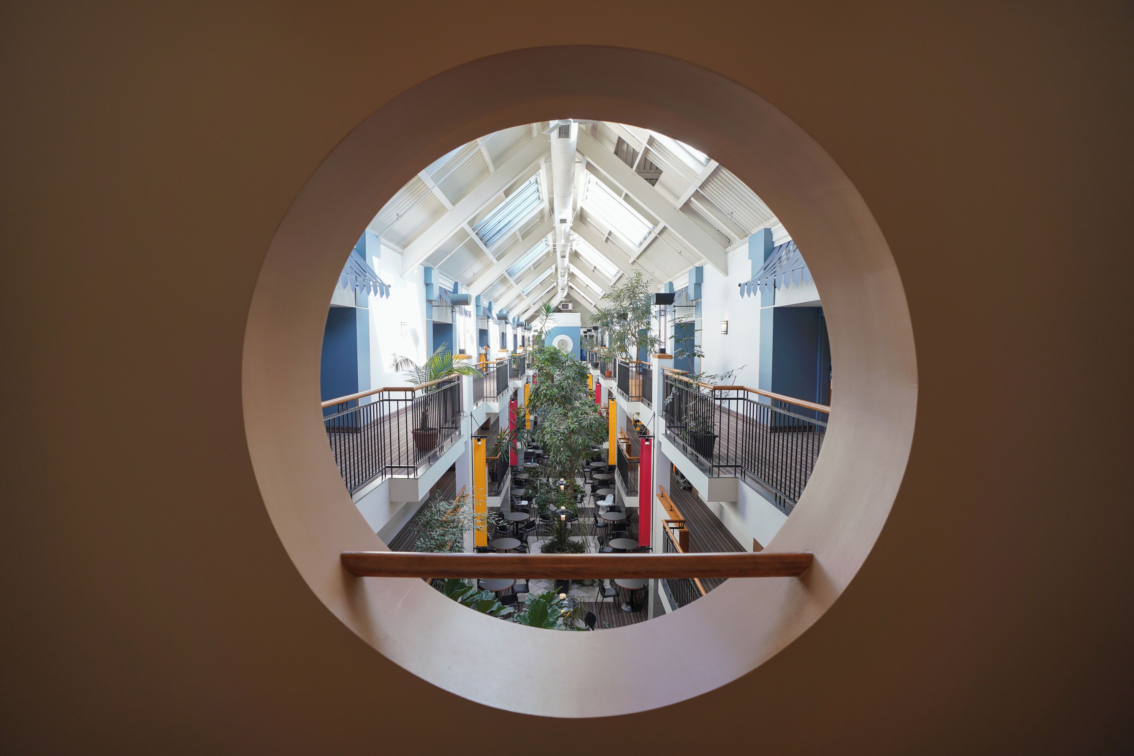 A circular view of a multi-level atrium with a central staircase, railings, and potted plants.